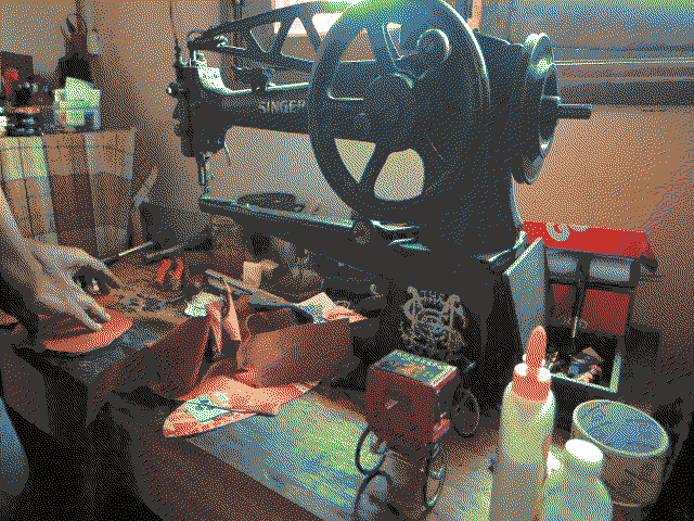 Léon en train de travailler sur un morceau de cuir pour faire un étui à lunettes, devant une vieille machine à coudre le cuir Singer posée sur son établi.