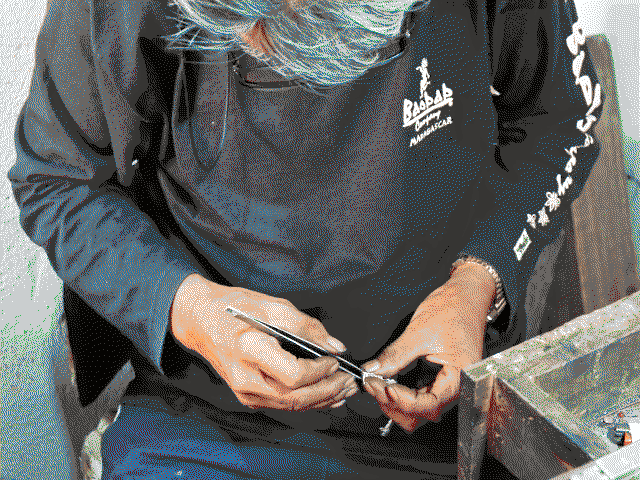 Papi en train de travailler sur un bracelet en argent à l'aide d'une pince à épiler.