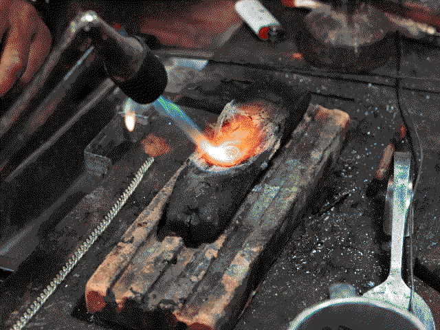 Argent en train de fondre sous la chaleur d'un chalumeau dans un creuset en bois.