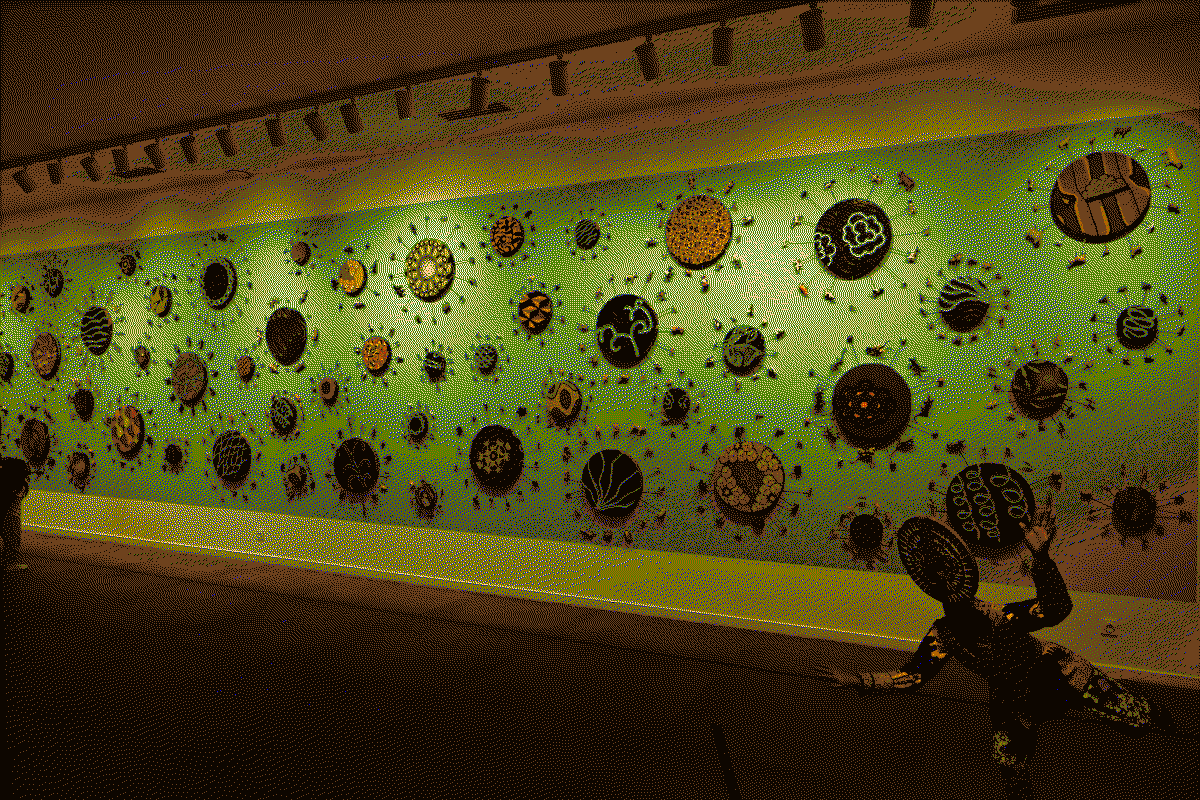 Photo de l'oeuvre accueillant les visiteurs. Un mur entier est peint en bleu ciel sur lequel des cercles de wax ornés de rayons au bout sont fixés des animaux