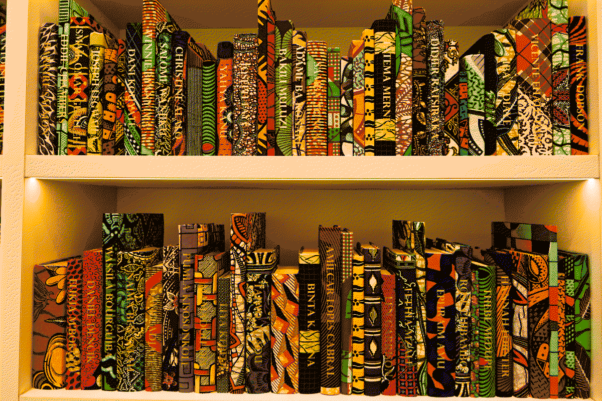 Photo d'une bibliothèque remplie de livres dont les couvertures sont recouvertes de tissu wax et sur les tranches desquelles sont écrits les noms de personnalités ayant façonné l'Afrique post-coloniale