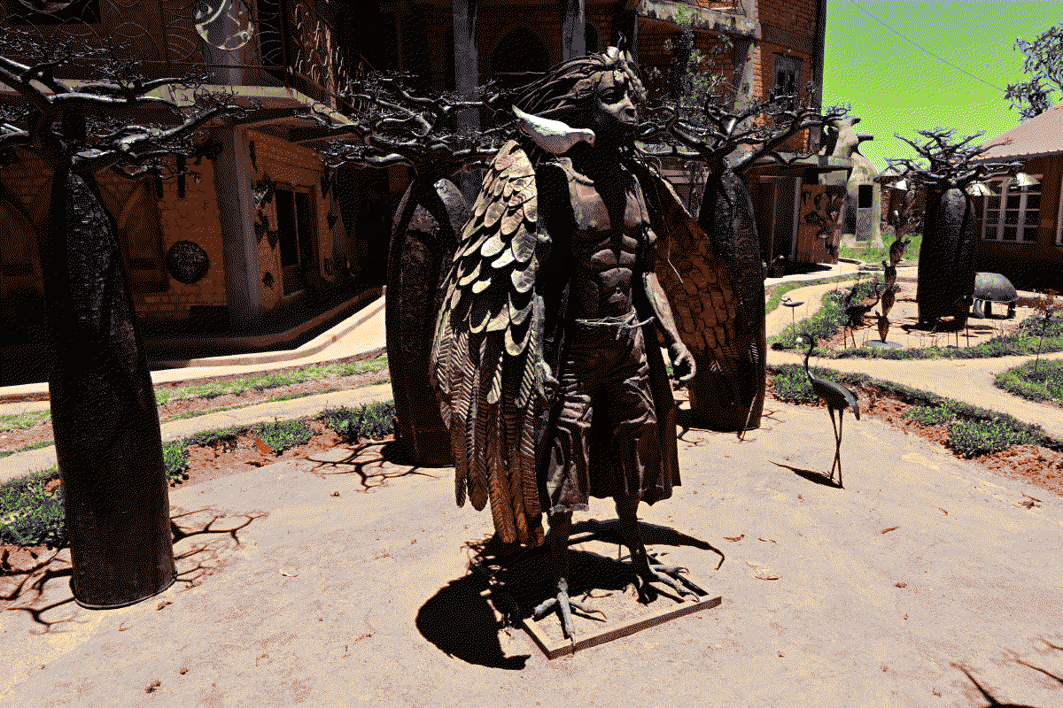Photo d'une statue de métal installée à l'extérieur représentant une divinité protectrice de la faune et de la flore malgache réalisée par Fitiavana Rakoto, la statue est entourée de deux grands baobabs en métal, pièces emblématiques du travail de Donné Vy
